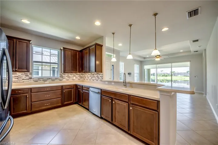 Kitchen with dishwasher, sink, light tile patterned flooring, kitchen peninsula, and decorative light fixtures