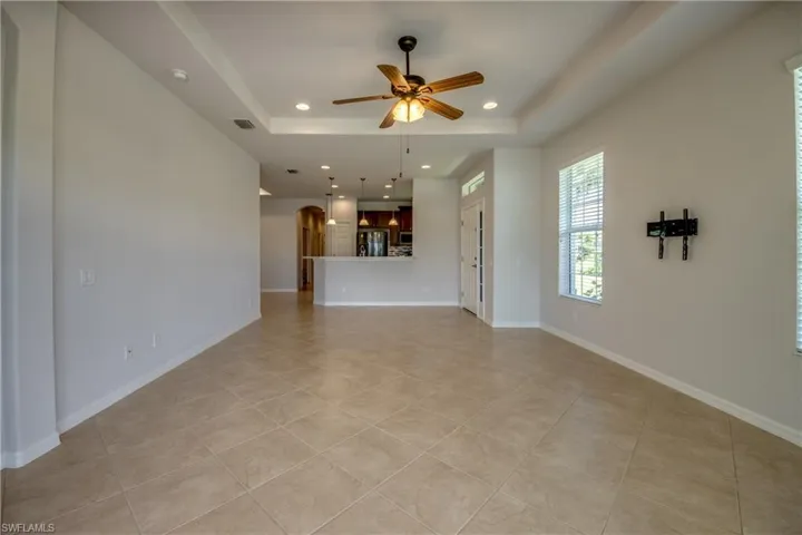Unfurnished living room with a tray ceiling, light tile patterned floors, and ceiling fan