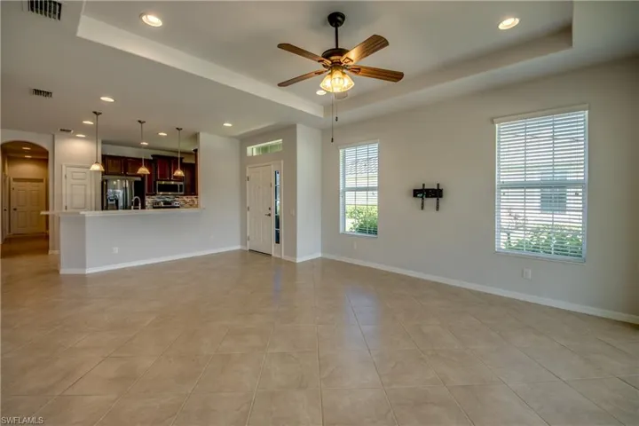 Unfurnished living room with ceiling fan, light tile patterned flooring, and a tray ceiling