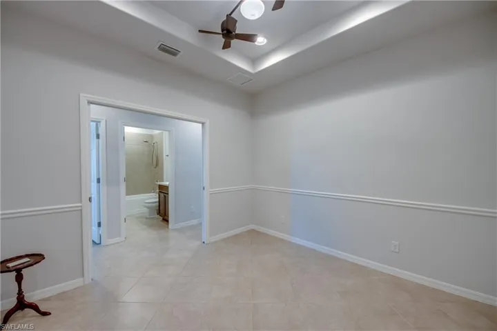 Tiled empty room featuring a tray ceiling and ceiling fan