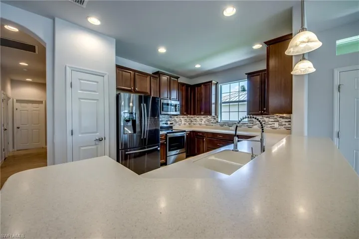 Kitchen featuring decorative backsplash, appliances with stainless steel finishes, pendant lighting, light wood-type flooring, and sink