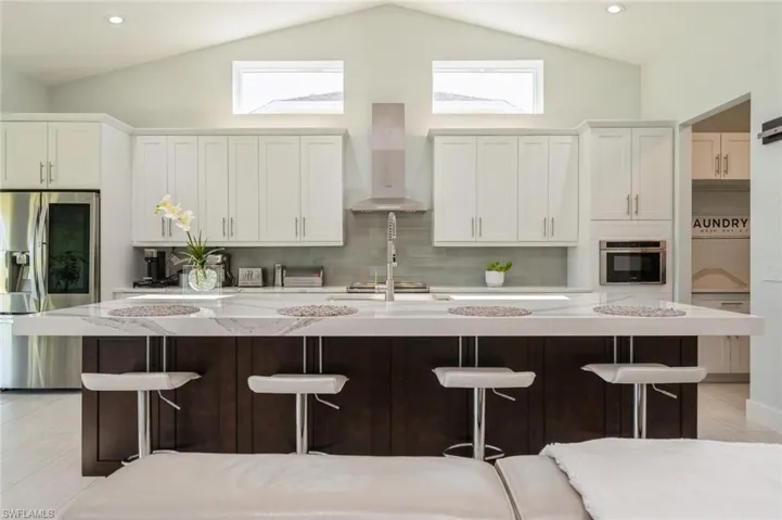 Kitchen with white cabinets, a kitchen bar, appliances with stainless steel finishes, vaulted ceiling, and wall chimney exhaust hood