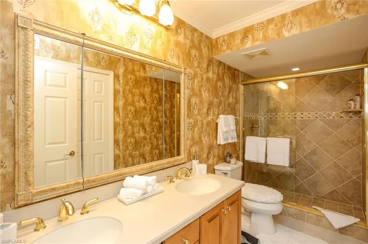 Bathroom with double vanity, a shower stall, wallpapered walls, and crown molding