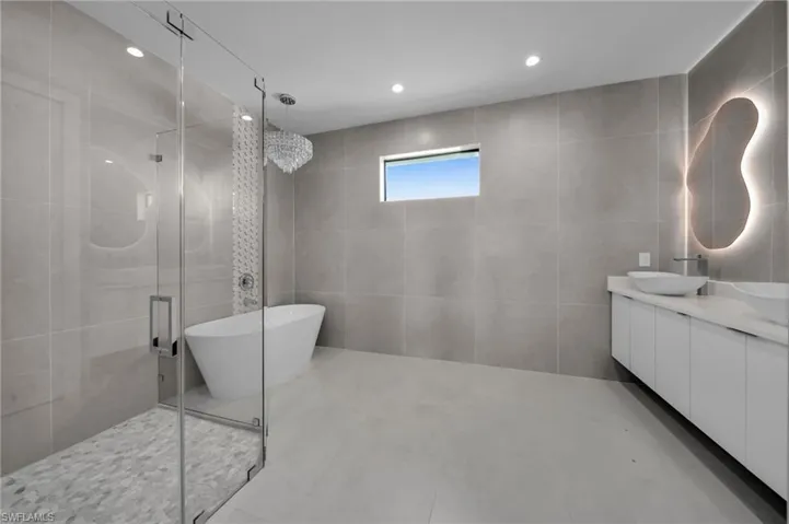 Full bathroom featuring a stall shower, double vanity, tile walls, a soaking tub, and recessed lighting