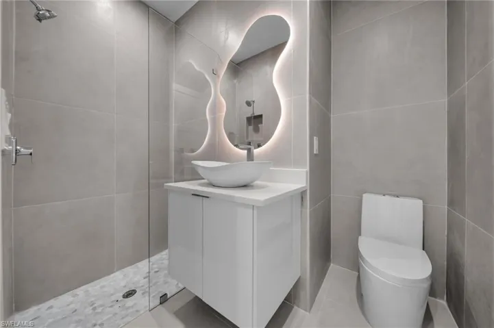 Full bathroom with vanity, tile walls, a tile shower, and tile patterned floors