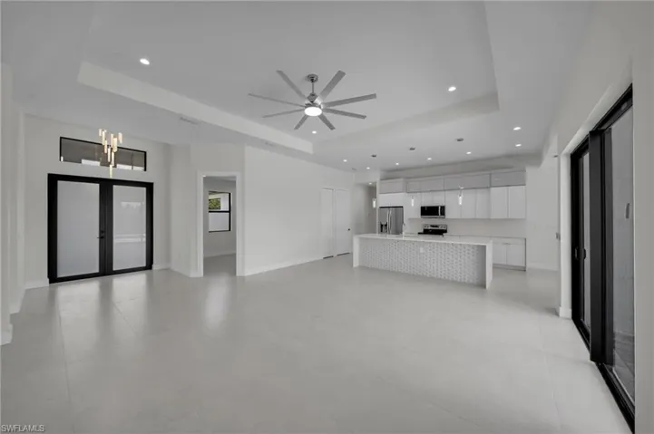 Unfurnished living room with a tray ceiling, recessed lighting, ceiling fan, a chandelier, and french doors