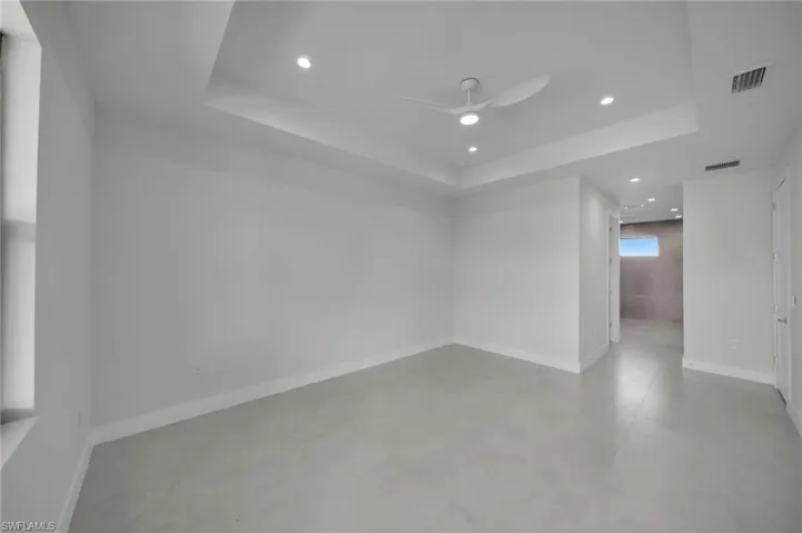 Empty room with a tray ceiling, a ceiling fan, concrete floors, and recessed lighting