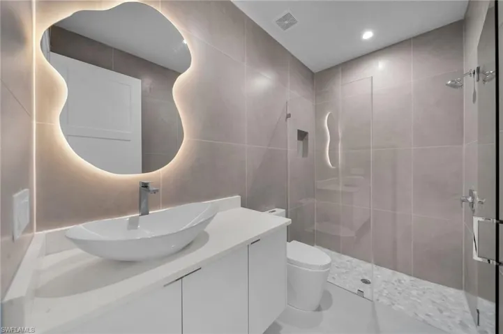 Bathroom featuring vanity, a tile shower, tile walls, and recessed lighting