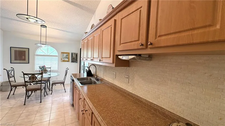 Kitchen featuring solid-surface  counters, textured ceiling, light tile patterned flooring, tasteful backsplash, and decorative light fixtures.