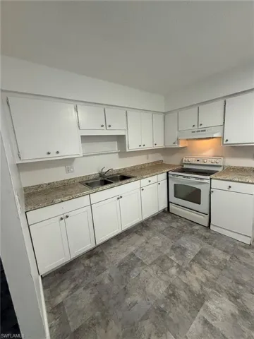 Kitchen with electric stove, white cabinetry, under cabinet range hood, and stone finish flooring