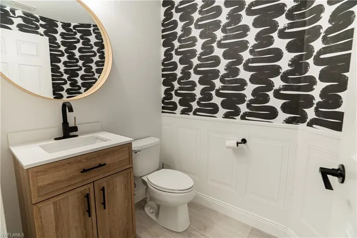 Half bathroom with vanity, wallpapered walls, and wainscoting