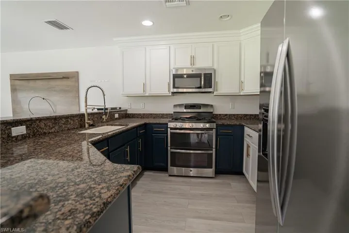 Dual tone kitchen featuring stainless steel appliances, dark stone countertops, recessed lighting, a peninsula, and light wood-style flooring