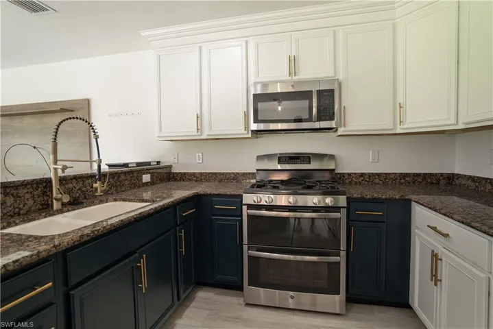 Kitchen featuring stainless steel appliances, dark stone countertops, and two tone cabinets