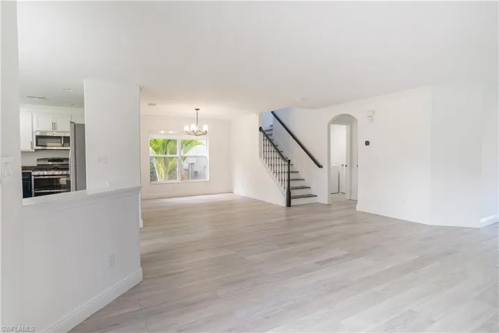 Unfurnished living room with hanging lights, light wood-style floors, arched walkways, and crown molding