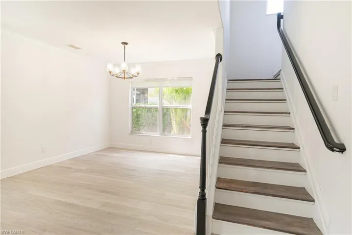 Stairway with hanging lights, ornamental molding, and wood finished floors