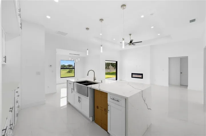 Kitchen with white cabinetry, light tile patterned floors, a tray ceiling, light stone countertops, and pendant lighting