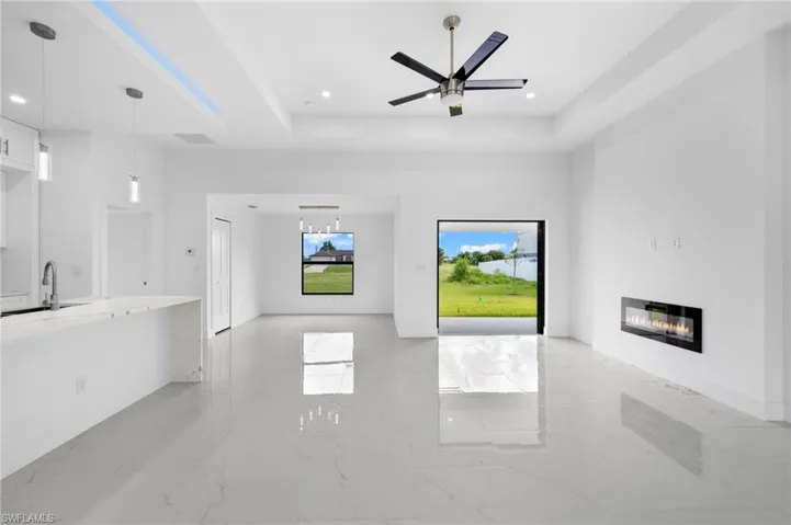 Unfurnished living room featuring sink, light tile patterned flooring, ceiling fan, and a raised ceiling