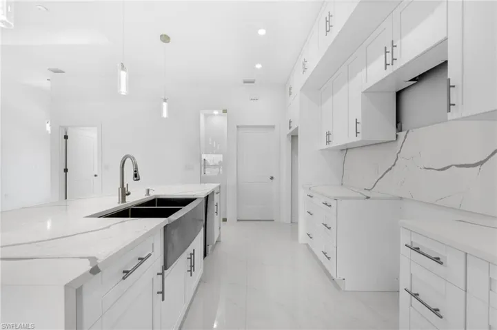 Kitchen with decorative light fixtures, light tile patterned flooring, white cabinets, sink, and light stone countertops