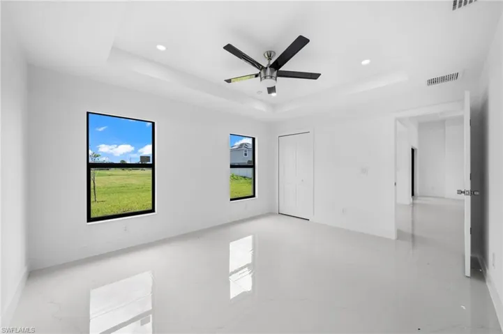 Empty room featuring ceiling fan, light tile patterned floors, and a tray ceiling