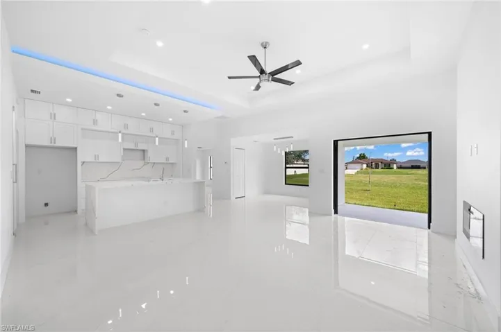 Unfurnished living room with ceiling fan, light tile patterned floors, and a tray ceiling