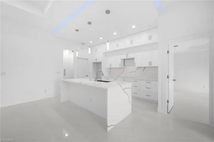 Kitchen featuring sink, light stone counters, light tile patterned floors, decorative backsplash, and white cabinetry