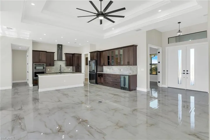 Unfurnished living room with french doors, a ceiling fan, wine cooler, light marble finish floors, and recessed lighting