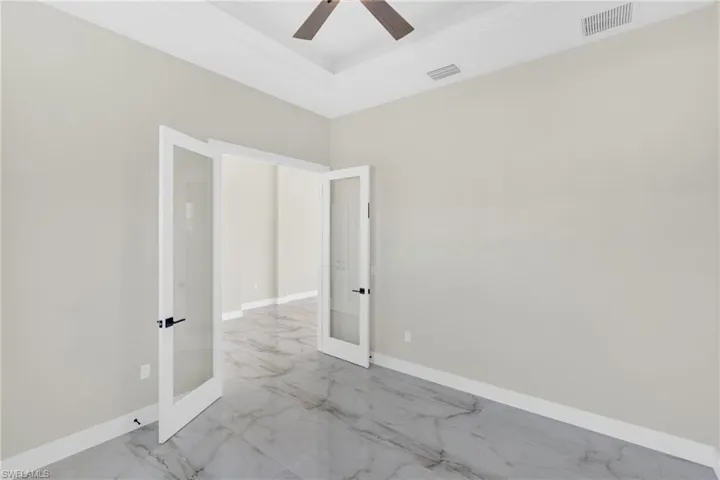Spare room with french doors, a ceiling fan, a raised ceiling, and light marble finish flooring