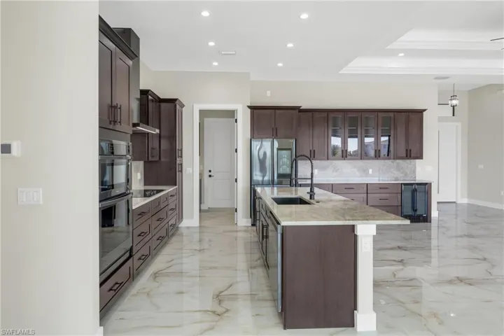Kitchen with glass fronted cabinets, light stone countertops, a tray ceiling, dark wood finish cabinets, and hanging light fixtures