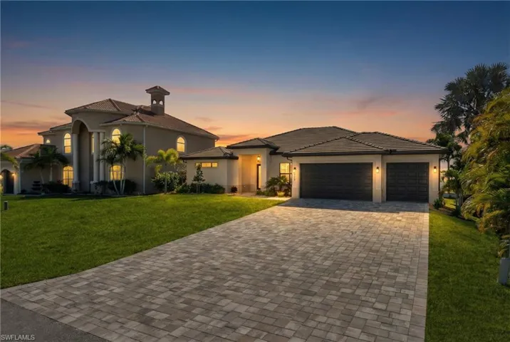View of front of house featuring a yard, decorative driveway, stucco siding, and an attached garage