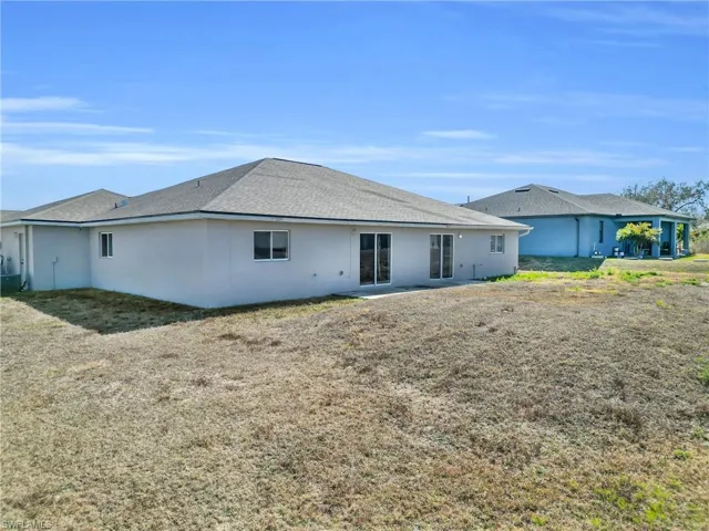 Back of property with a shingled roof, stucco siding, a patio, and a yard