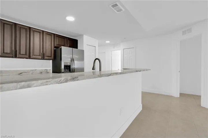 Kitchen with stainless steel refrigerator with ice dispenser, dark wood finish cabinetry, recessed lighting, light stone counters, and light tile patterned floors