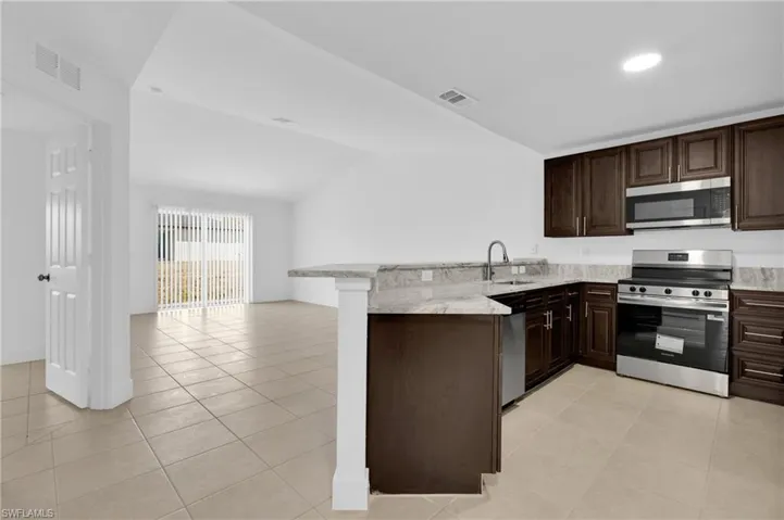 Kitchen with a peninsula, stainless steel appliances, dark wood finish cabinets, light tile patterned flooring, and open floor plan