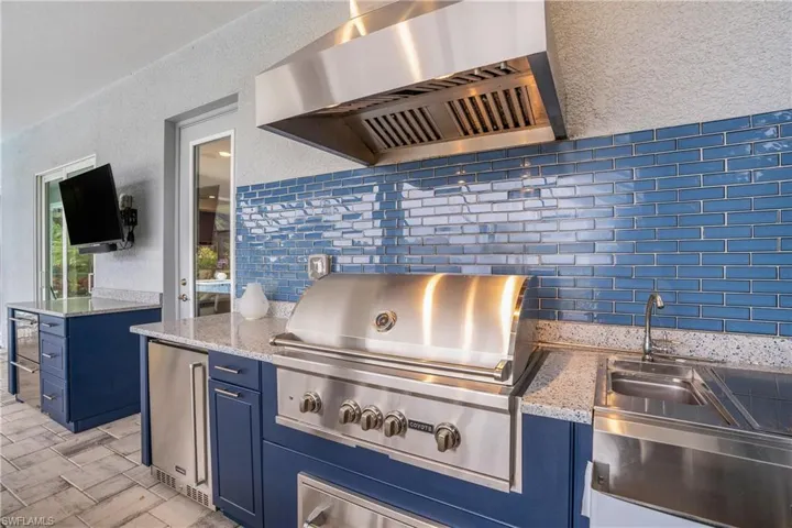 Kitchen featuring decorative backsplash, fridge, blue cabinets, wall chimney exhaust hood, and light stone counters