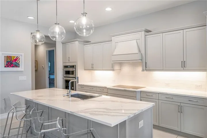 Kitchen with pendant lighting, stainless steel double oven, black electric stovetop, sink, and a center island with sink