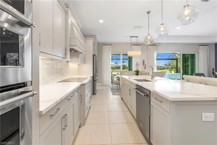 Kitchen featuring stainless steel appliances, decorative backsplash, a spacious island, pendant lighting, and sink