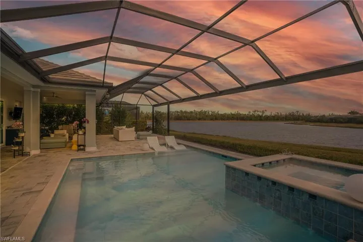 Pool at dusk with a lanai, a water view, an in ground hot tub, and a patio