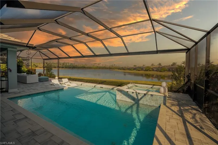 Pool at dusk featuring an in ground hot tub, a water view, a patio, a lanai, and an outdoor living space