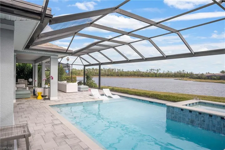 View of swimming pool featuring a patio area, an in ground hot tub, glass enclosure, a water view, and an outdoor hangout area