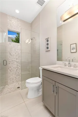 Bathroom with a shower with shower door, tile patterned floors, toilet, and vanity