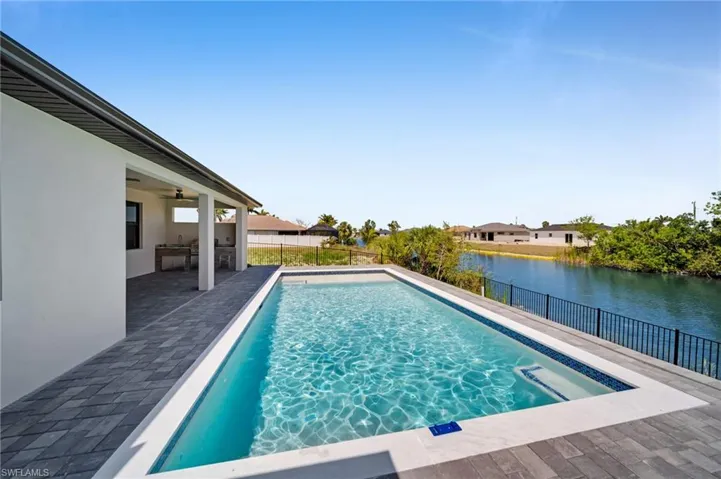 View of swimming pool with a fenced in pool, a fenced backyard, a water view, a patio area, and a ceiling fan