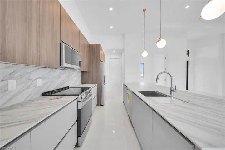 Kitchen featuring a sink, modern cabinets, decorative backsplash, light stone countertops, and appliances with stainless steel finishes