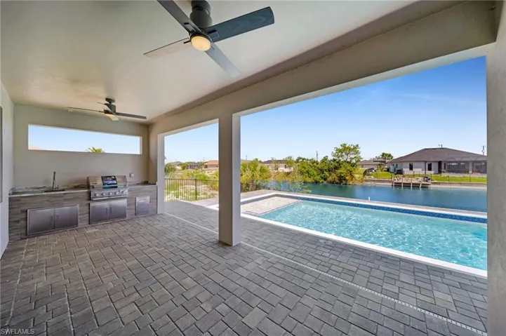 Pool with a patio area, a water view, a ceiling fan, a grill, and area for grilling
