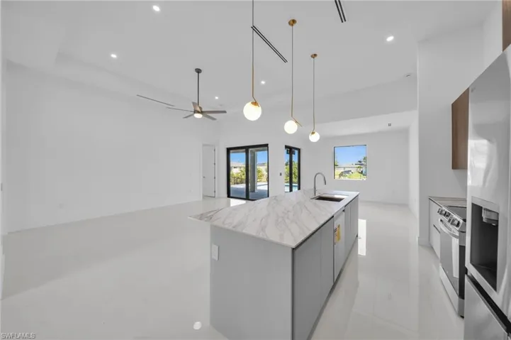 Kitchen with a kitchen island with sink, a sink, modern cabinets, appliances with stainless steel finishes, and hanging light fixtures