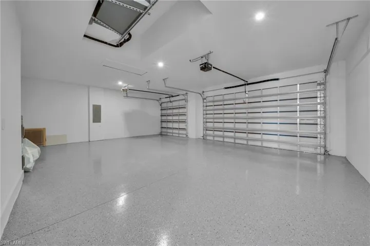 Garage with electric panel, recessed lighting, and a garage door opener