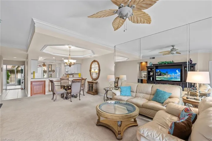 Living room featuring a ceiling fan, ornamental molding, light carpet, and a tray ceiling