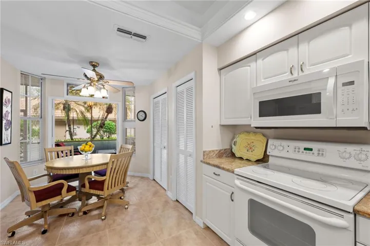 Kitchen with white appliances, white cabinets, light tile patterned flooring, and a ceiling fan