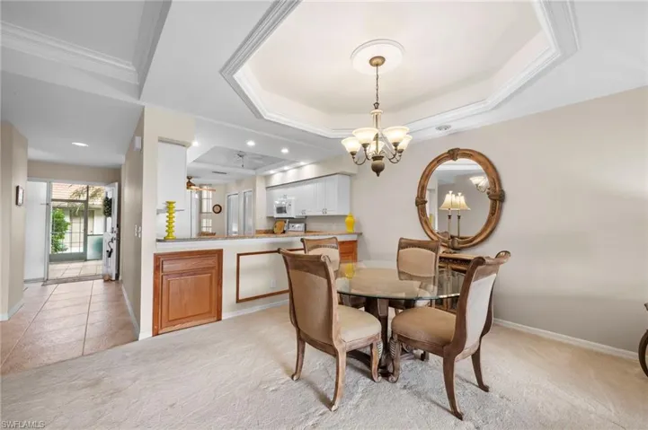 Dining space featuring a ceiling fan, a chandelier, light carpet, light tile patterned floors, and a raised ceiling