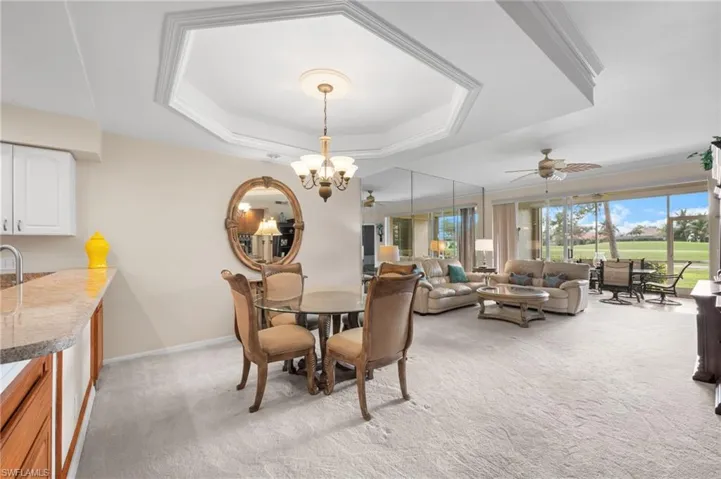 Dining area featuring light carpet, a tray ceiling, a chandelier, and a ceiling fan