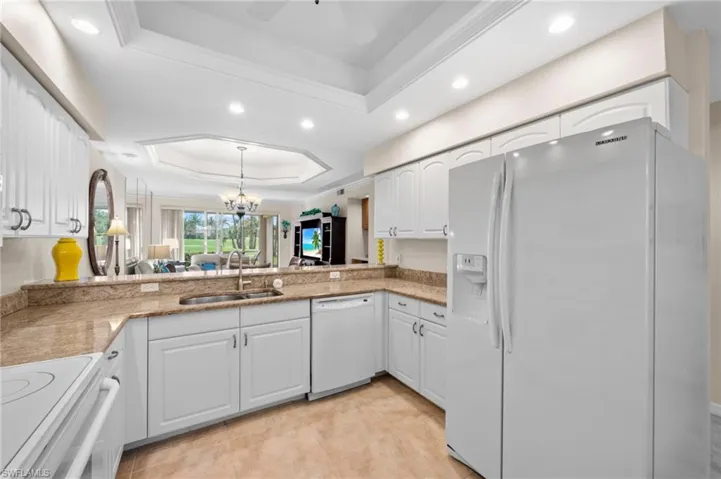 Kitchen with white appliances, a raised ceiling, white cabinetry, a chandelier, and recessed lighting