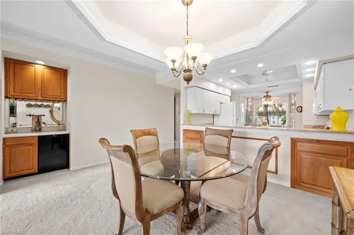 Dining space with light carpet, a tray ceiling, a chandelier, recessed lighting, and ornamental molding